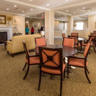 A cozy lounge area with tables and chairs, featuring a carpeted floor and a warm ambiance.