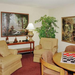 A cozy living room with comfortable chairs, a table with a checkerboard, and decorative artwork on the walls.