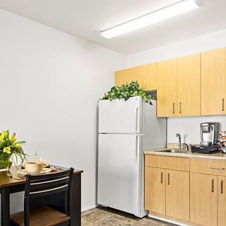 A compact kitchen area with light wooden cabinets, a white refrigerator topped with plants, and a small dining table decorated with flowers.