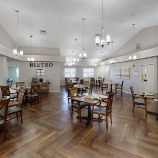A spacious bistro dining area with elegant chandeliers, wooden flooring, and neatly arranged tables and chairs.