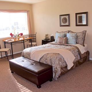 A cozy bedroom with a neatly made bed, a small dining table by the window, and elegant decor.