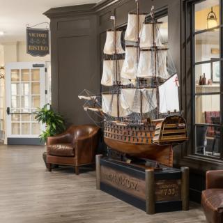 A model ship displayed in a lobby with nautical-themed interior decor, featuring leather chairs and wood flooring.
