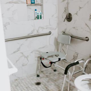 Accessible bathroom featuring a shower chair and grab bars for safety.