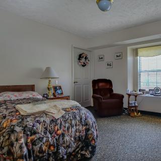 A cozy bedroom with a bed, upholstered chair, and a large window allowing natural light.
