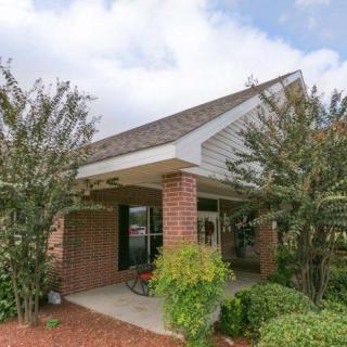 A cozy brick house with a covered porch, surrounded by shrubs and trees.