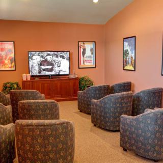 A cozy lounge area with plush chairs facing a large television, surrounded by framed posters on the walls.