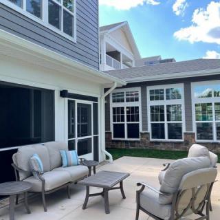 A cozy outdoor patio area with comfortable seating and a small table, set against the backdrop of a modern house on a sunny day.
