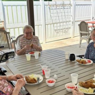A group of elderly individuals enjoying a meal together outdoors on a sunny day.
