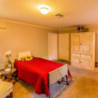 A cozy bedroom with a single bed covered in a red blanket, featuring a wardrobe and a side table with a lamp.