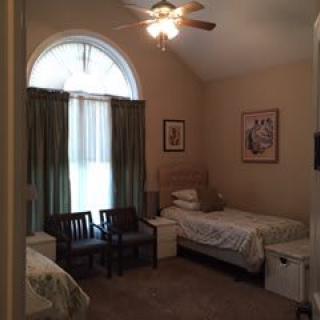 A cozy bedroom with a single bed, chairs, and a large window with curtains.