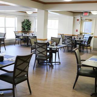 An empty dining area with neatly arranged tables and chairs, illuminated by natural light through large windows.
