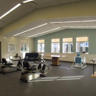 A spacious gym with various exercise equipment and large windows allowing natural light.