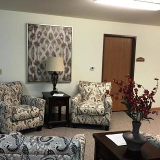 A cozy living room setup featuring patterned chairs, a side table with a lamp, and decorative elements including wall art and a vase of flowers.