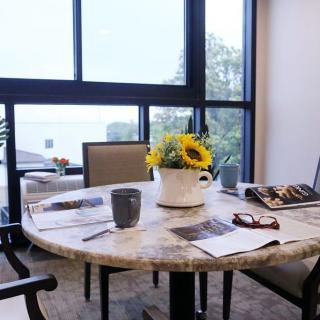 A cozy table setup with sunflowers, magazines, and a coffee mug near a large window.