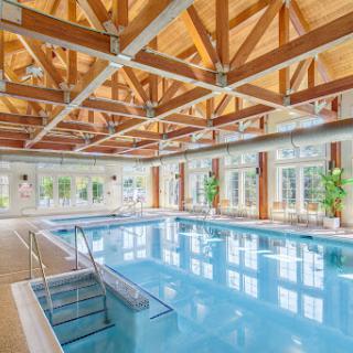 A beautifully designed indoor swimming pool with wooden beams and ample natural light.