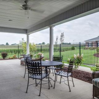 A covered patio with a set of metal chairs and a table overlooking a landscaped garden.