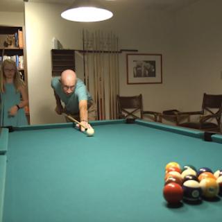 A man prepares to take a shot at the pool table while a woman watches.