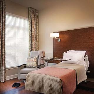 A cozy hospital room with a single bed, chair, and a large window.