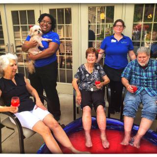 A group of people, including seniors, relaxing outdoors with drinks and a small pool.