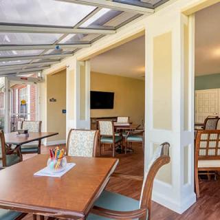 A bright indoor dining area with wooden tables and chairs, featuring a glass ceiling and a television on the wall.