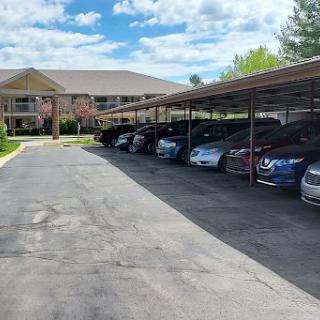 A row of cars parked under a covered area in a residential complex, surrounded by a clear blue sky.