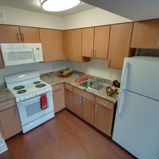A modern kitchen with wooden cabinets, a refrigerator, stove, microwave, and sink.