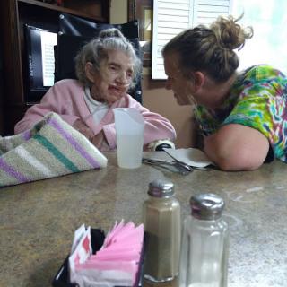 A joyful moment shared between an elderly woman and her caregiver, highlighting warmth and connection over a table.