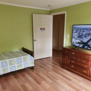 A bedroom with green walls, featuring a bed, a wooden dresser with a television on top, and hardwood flooring.