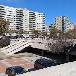 A view of a modern urban landscape featuring residential buildings and a parking area under bright blue skies.