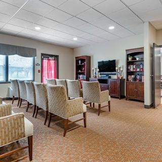 A spacious room with rows of chairs facing a television, flanked by bookshelves and featuring carpeted flooring.