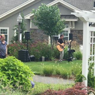 A musician performs outdoors in a garden setting near a house.