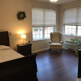 A cozy bedroom with large windows, a comfortable chair, and a neatly made bed.