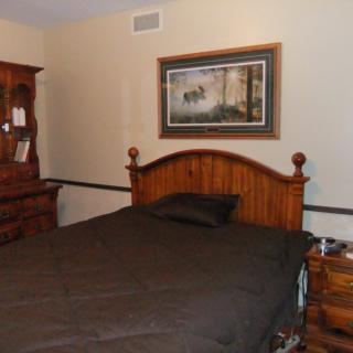 A cozy bedroom featuring a bed with a wooden headboard, a dresser, and a framed painting on the wall.