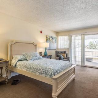 A cozy, well-lit bedroom with a bed, lamp, and chair near the window.