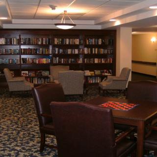 A cozy library room with bookshelves, comfortable chairs, and a table.