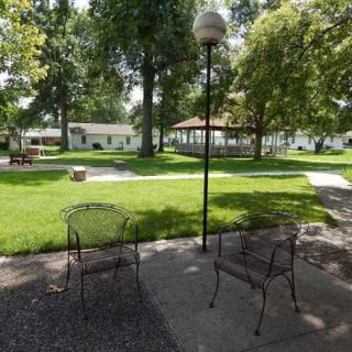 A serene park setting with two metal chairs, a lamp post, and a gazebo in the distance.