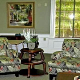 A cozy living room with floral chairs, a small table, and decorative elements like a plant and a painting.
