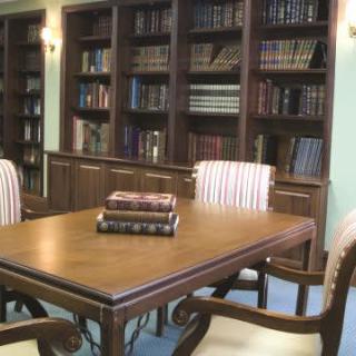 A cozy library with a wooden table surrounded by bookshelves and chairs.