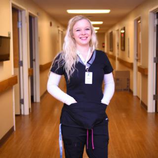 A healthcare professional in a hospital corridor, smiling and wearing a uniform.