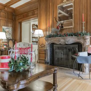 A cozy living room featuring wood paneling and a decorated fireplace, adorned with holiday decorations and elegant furnishings.