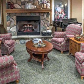 A cozy living room with armchairs arranged around a fireplace, featuring a wooden coffee table and a green carpet.