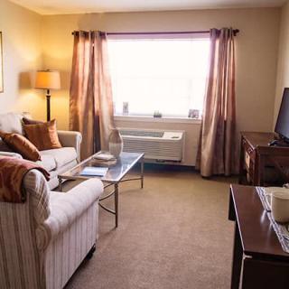 A cozy living room with a sofa, lamp, TV, and coffee table, featuring a large window with curtains.