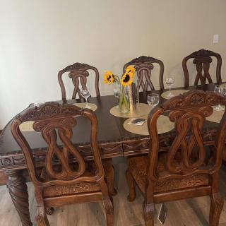 A wooden dining table set with six chairs, featuring a vase of sunflowers as the centerpiece.