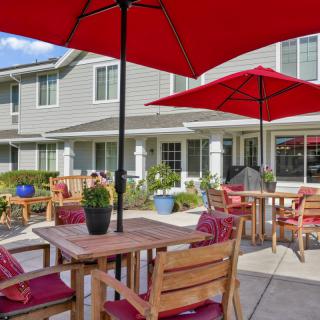 A cozy outdoor patio with wooden furniture and red umbrellas, set against a building backdrop.