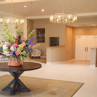 A modern lobby featuring elegant chandeliers and a vibrant floral arrangement on a central table.