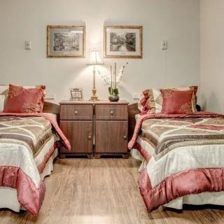 A cozy bedroom features twin beds with matching bedding and a central nightstand, illuminated by a lamp and adorned with artwork on the walls.