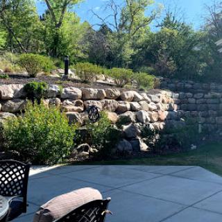 A peaceful outdoor garden scene featuring a rocky wall, lush greenery, and a patio area.