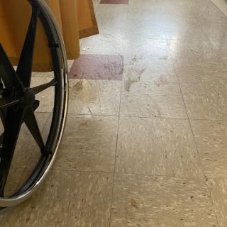 A close-up view of a wheelchair positioned next to a polished floor, possibly in a healthcare setting.