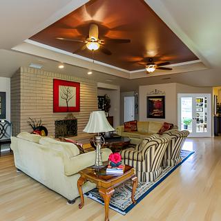 A spacious and well-lit living room featuring cozy sofas, a coffee table, ceiling fans, and artwork on the walls.