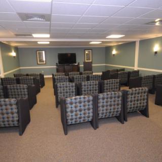 A small theater room with rows of upholstered chairs facing a television.